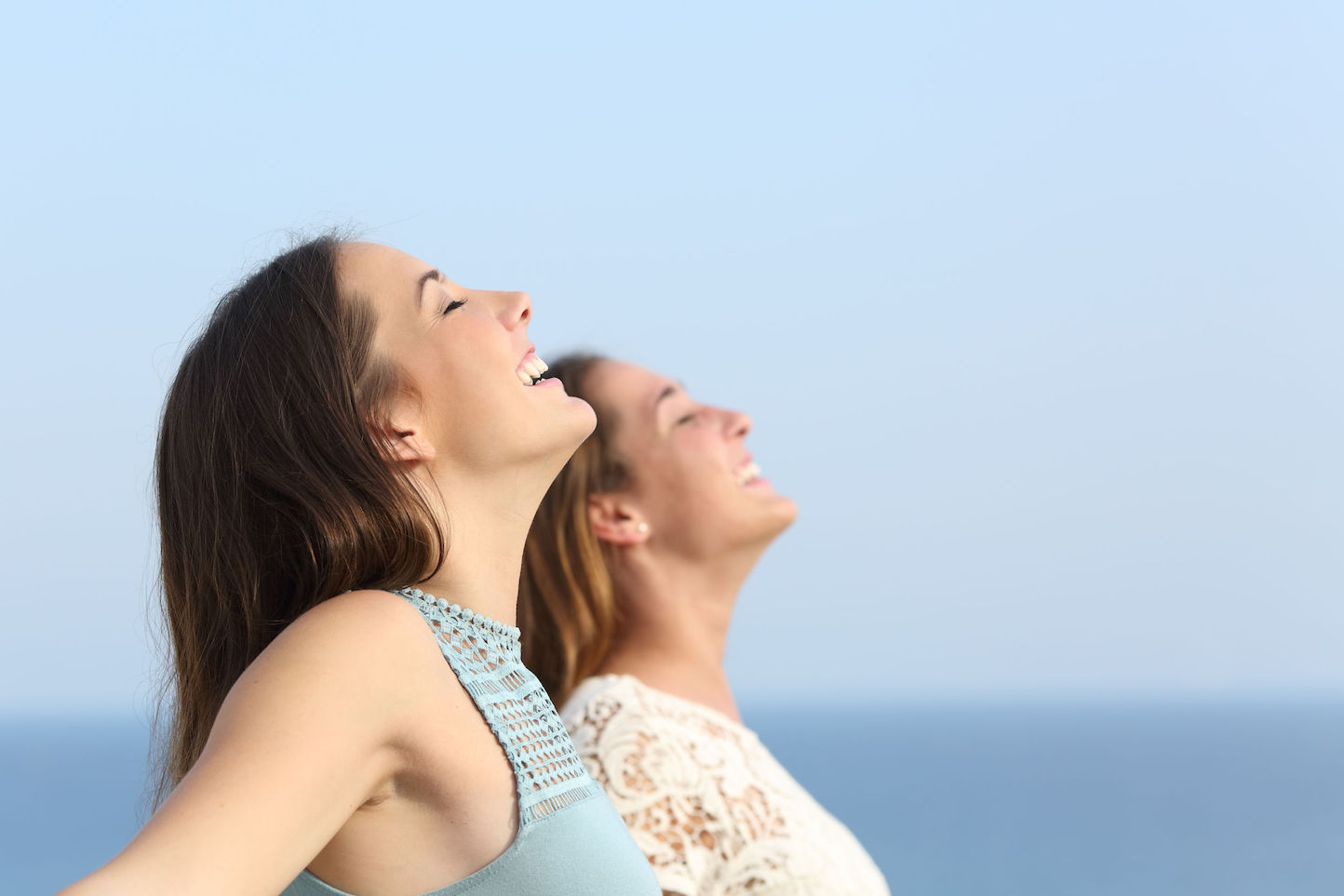Two girls doing breath exercises inhaling fresh air on the beach